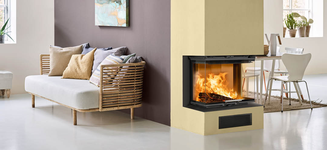 Een geel geverfde open haard in een witte kamer met aan de ene kant een keuken en aan de andere kant een bank