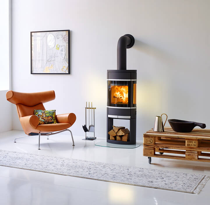 Zwarte haard Scan 68 brandend in een witte kamer met een cognackleurige stoel en een pallettafel ernaast