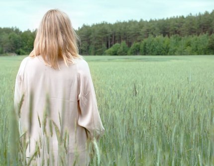 Blonde vrouw in witte jurk staande in een groen veld