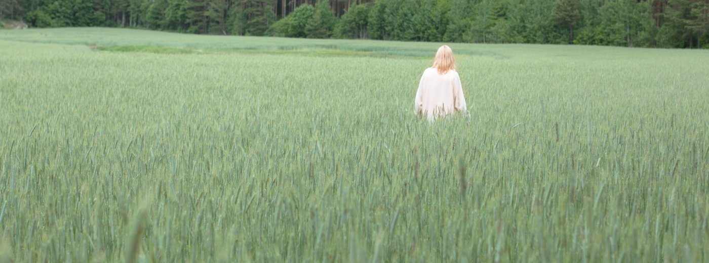 Blonde vrouw in witte jurk staande in een groen veld