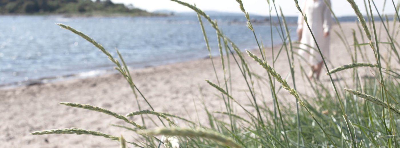 Vrouw in witte jurk die langs een Deens strand loopt